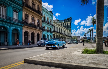 Naklejka na ściany i meble HDR - Amerikanischer blauer Chevrolet Oldtimer fährt an der historischen Häuserfront der Hauptstrasse vorbei in Havanna Kuba - Serie Kuba Reportage