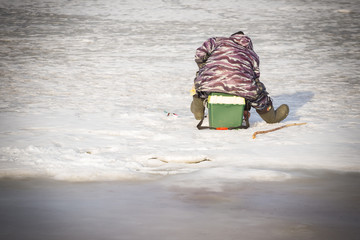 One fisherman on winter fishing sits on a box and catches fish. On the river dangerous thin ice