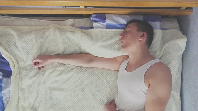 Top view of young man in a undershirt is sleeping in a bed with an open mouth