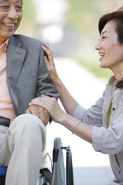 Mature woman and senior man on wheelchair holding hands