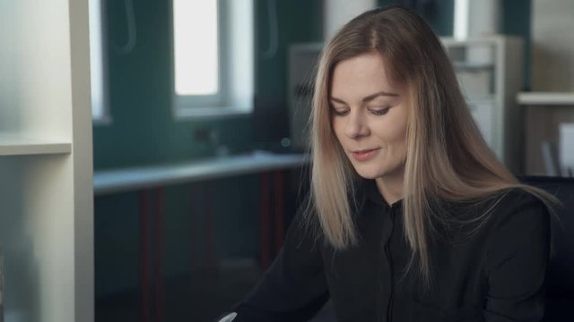 Manager discussing contract to enter with client inside office. blonde with long straight hair, black shirt says, explains conditions of cooperation for interlocutor indoors. Fair-haired woman sitting