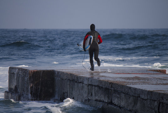 Surfer runs into water wearing a wetsuit in winter. Cold surfing. Wave splash. waterproof suit