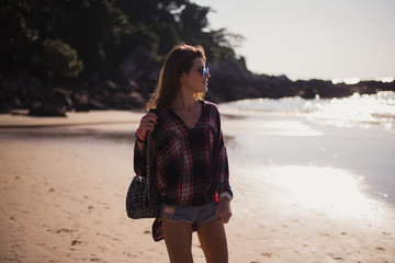 Summer sunny lifestyle fashion portrait of young stylish hipster woman walking on beach,wearing cute trendy outfit, travel, hikes, smiling enjoy her weekends