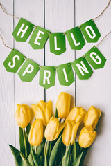 Yellow tulips bunch on white wooden planks rustic barn rural table backgropund. Hallo spring garland paper lettering, text, letters, inscription. Beautiful vertical flat lay postcard.