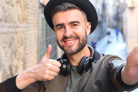 Trendy handsome man taking a selfie and giving a thumbs up outdoors 