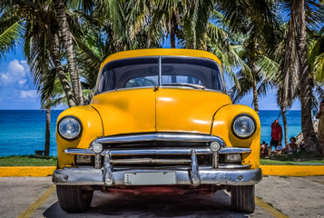 HDR - Gelber amerikanischer Oldtimer parkt unter Palmen am Strand in Varadero Kuba - Serie Kuba Reportage