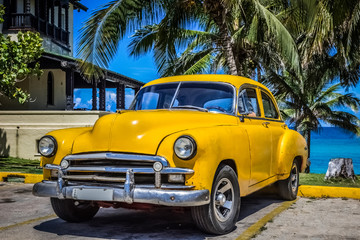 HDR - Gelber amerikanischer Oldtimer parkt unter Palmen am Strand in Varadero Kuba - Serie Kuba Reportage