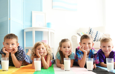 Cheerful children with glasses of milk lying on colourful carpet in the room