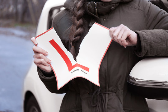 Happy young woman tearing learner driver sign while standing near car outdoors, closeup