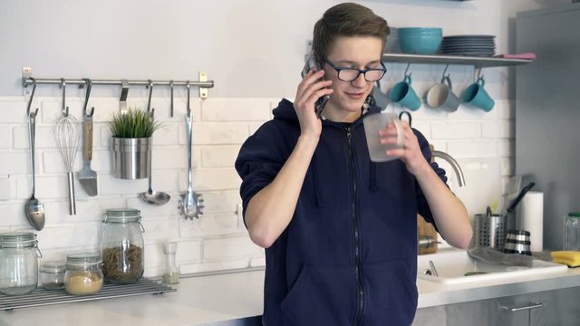 Young boy talking on cellphone and drinking water in kitchen
