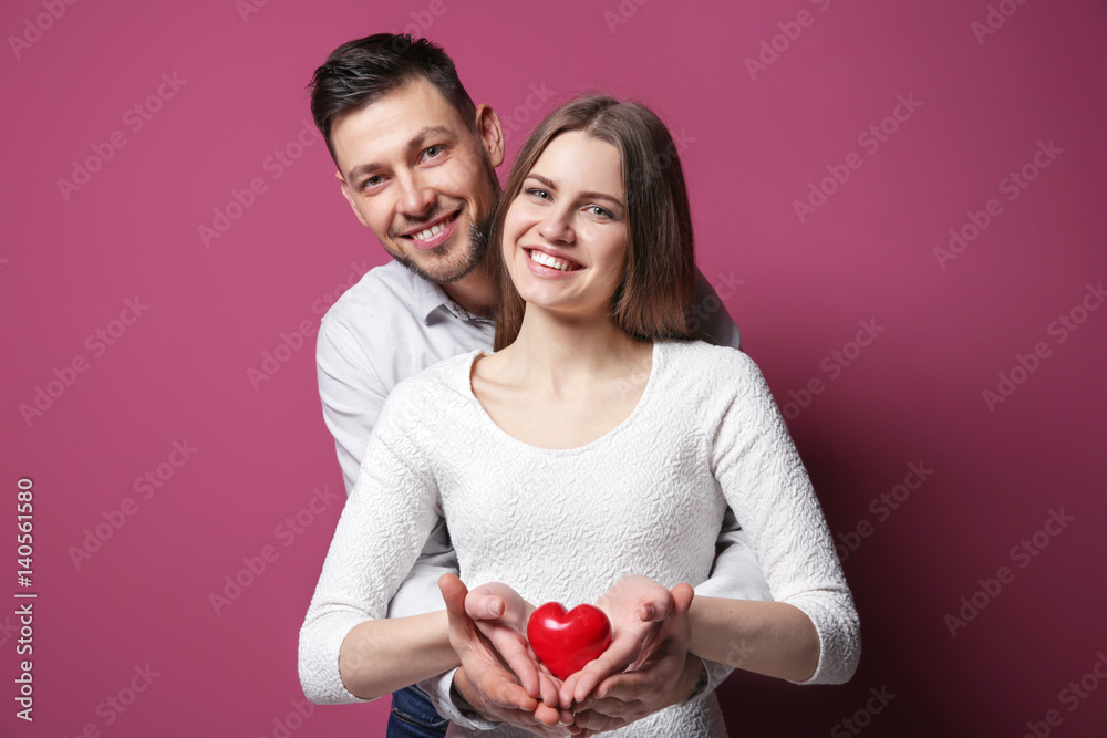 Poster Happy young couple with small red heart on color background