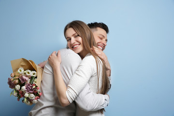 Happy young couple with bouquet of flowers on light background