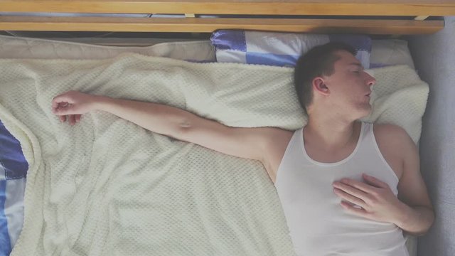 Top view of young man in a undershirt is sleeping in a bed and turns his head