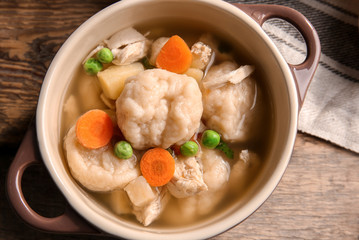 Ceramic pan with delicious chicken and dumplings on wooden kitchen table