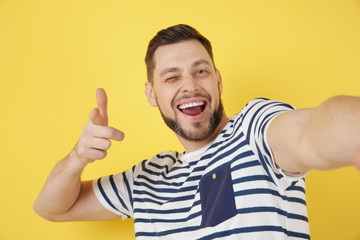 Handsome young man taking selfie on color background