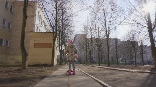 Little girl is riding on a scooter on a sunny day in the spring