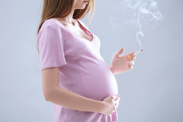 Pregnant woman smoking cigarette on grey background