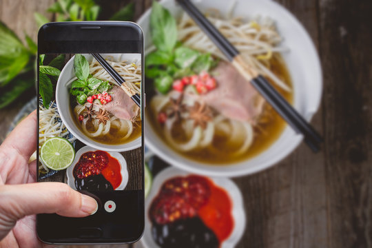 Taking a photo by Finger Pressing on Smartphone for Photograph Pho Vietnamse Noodle Soup on Wooden Background with Copy Space. Image for Food Advertise Concept