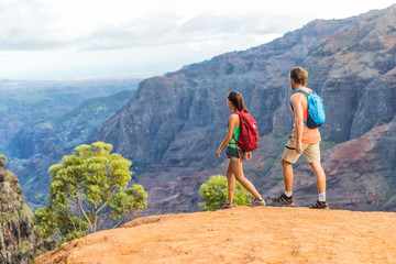 Hikers couple hiking in mountains landscape. Woman and man walking on hike in Waimea Canyon State Park, Kauai, Hawaii, USA. Looking at view happy enjoying healthy outdoor lifestyle. - obrazy, fototapety, plakaty