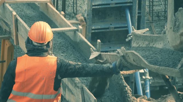 Construction worker stands at the conveyor, along which liquid concrete is delivered to the construction site