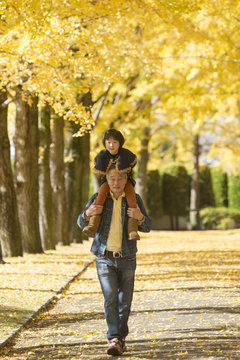 Grandfather carrying granddaughter on shoulders in autumn