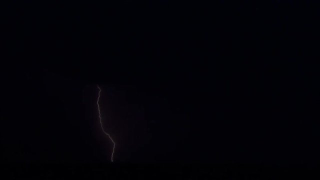 Night lightning bolts striking in rapid succession above low hills