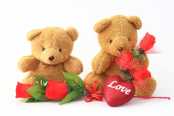 Brown teddy bear holding two roses on a white background.