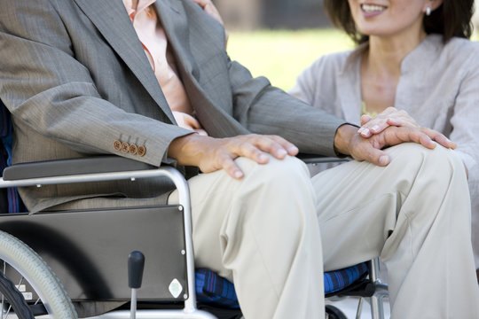 Mature woman and senior man on wheelchair holding hands