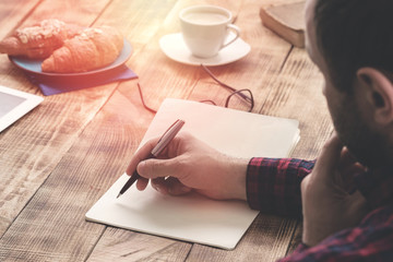 Male hands writing on notebook sitting at coffee shop