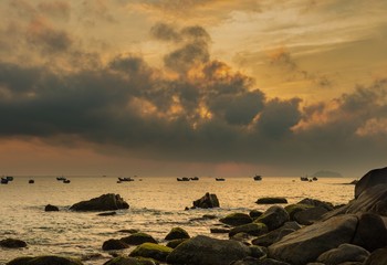 Fototapeta premium A fiery orange morning sky looking out over the south China sea in Vung Lam Bay Vietnam. With a rock covered coastline and fishing boat silhouettes.