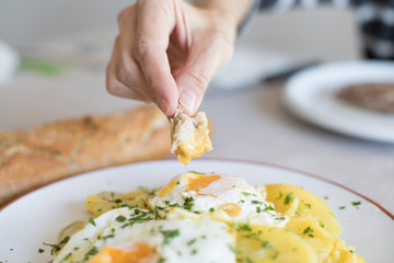 woman hand with piece of bread dipping in fried yolk egg of typical Spanish food, with sliced fried potatoes, and chopped parsley
