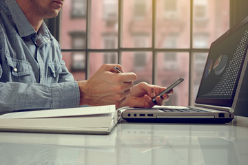 Side view shot of a man's hands using smart phone in interior, rear view of business man hands busy using cell phone at office desk, young male student typing on phone sitting at white table, flare