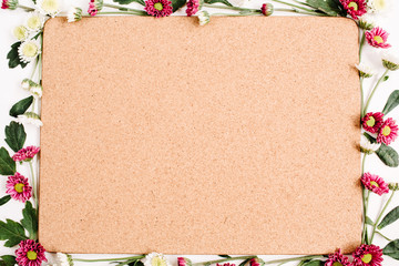 Frame with red and white wildflowers, green leaves, branches and wooden cork tree board on white background. Flat lay, top view. Flower background.