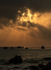 Fototapeta premium A fiery orange morning sky looking out over the south China sea in Vung Lam Bay Vietnam. With a rock covered coastline and fishing boat silhouettes.