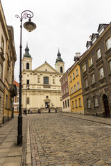 Fototapeta na wymiar The area of the Old Town in Warsaw, Poland . An old street with nineteenth-century houses, a street lamp and a baroque church.
