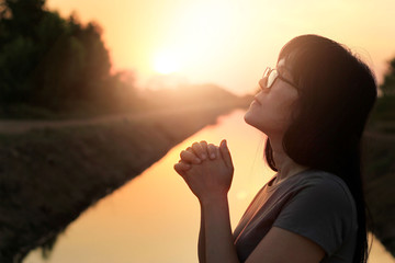 Naklejka premium Woman praying with hands together on nature sunset background