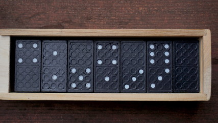 black dominoes in wooden box, on wooden background.