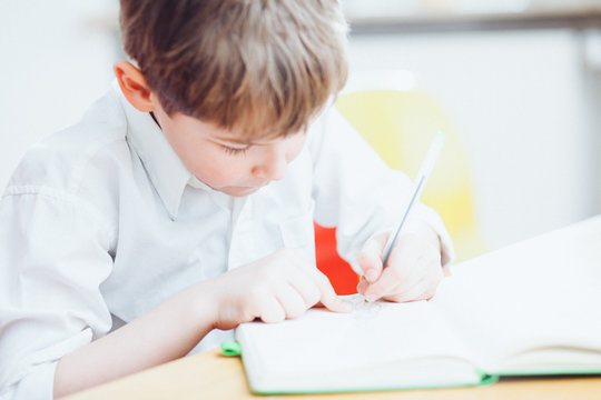 Left handed school boy writing or drawing in book