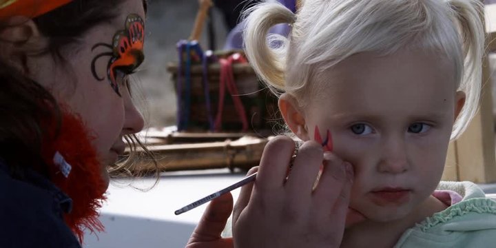 Carnival artist drawing a design on a little girl's face