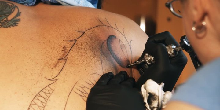 Tattoo artist inking a design on a customer's back