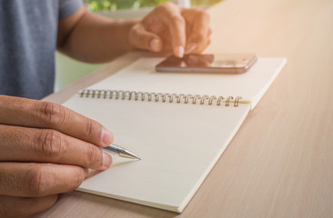 Man hand with pen writing on notebook and phone on notebook.