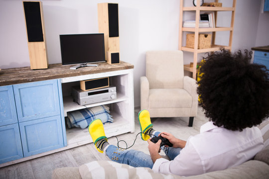 Hipster man sitting on sofa or couch and playing computer games in front of television at home. Happy man enjoying free time. Computer games concept.