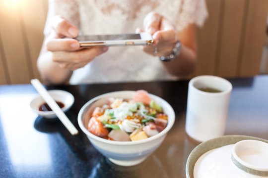 Blurred photo of young woman photographing Japanese food by her smartphone in Japanese restaurant.