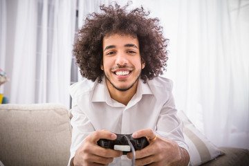 Happy, smiling, fun, entertainment, hands close up, details. Young hipster handsome bearded man sitting on couch at home, playing video game on laptop computer while holding joystick.