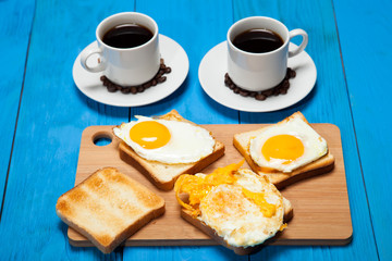 Two cups with coffee, toast and egg on a blue wooden table