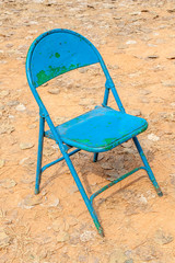 Old rusty blue chair leave alone in abandoned dried backyard.