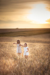 Sisters girls walk in the field with rye sunset