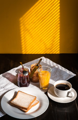 Fototapeta na wymiar Breakfast with peanut butter and jam and a cup of coffee on a wooden table in the morning sun