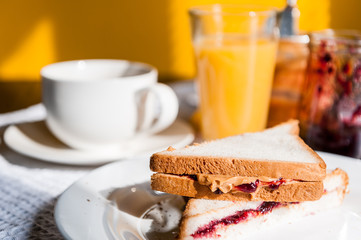 Breakfast with peanut butter and jam and a cup of coffee on a wooden table in the morning sun