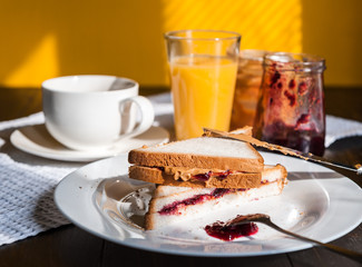 Breakfast with peanut butter and jam and a cup of coffee on a wooden table in the morning sun